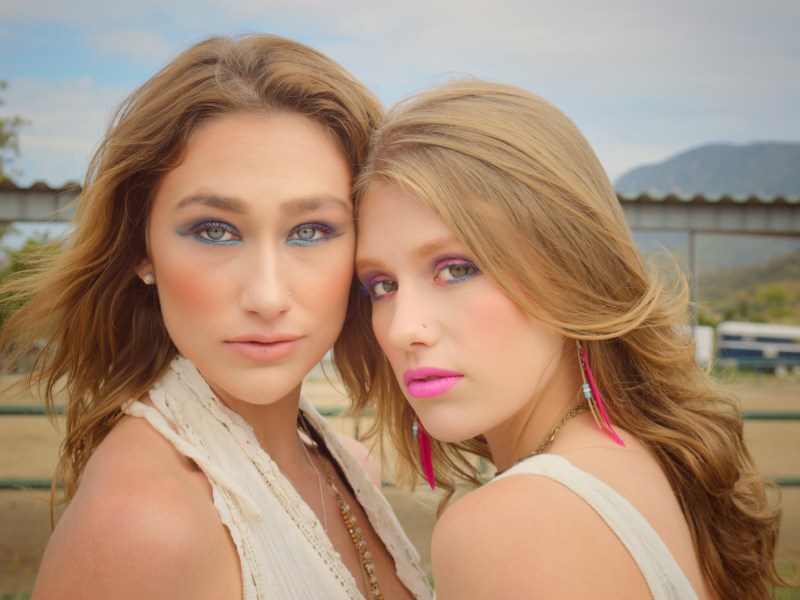 Two young women with 80’s style makeup posing face to face on a horse ranch