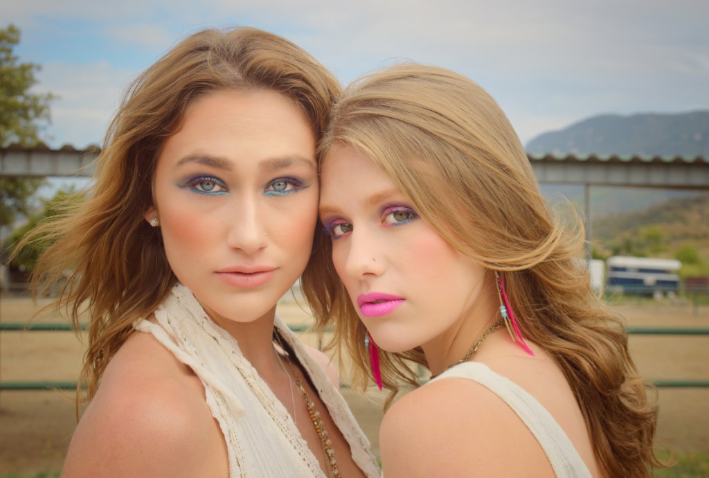Two young women with 80’s style makeup posing face to face on a horse ranch