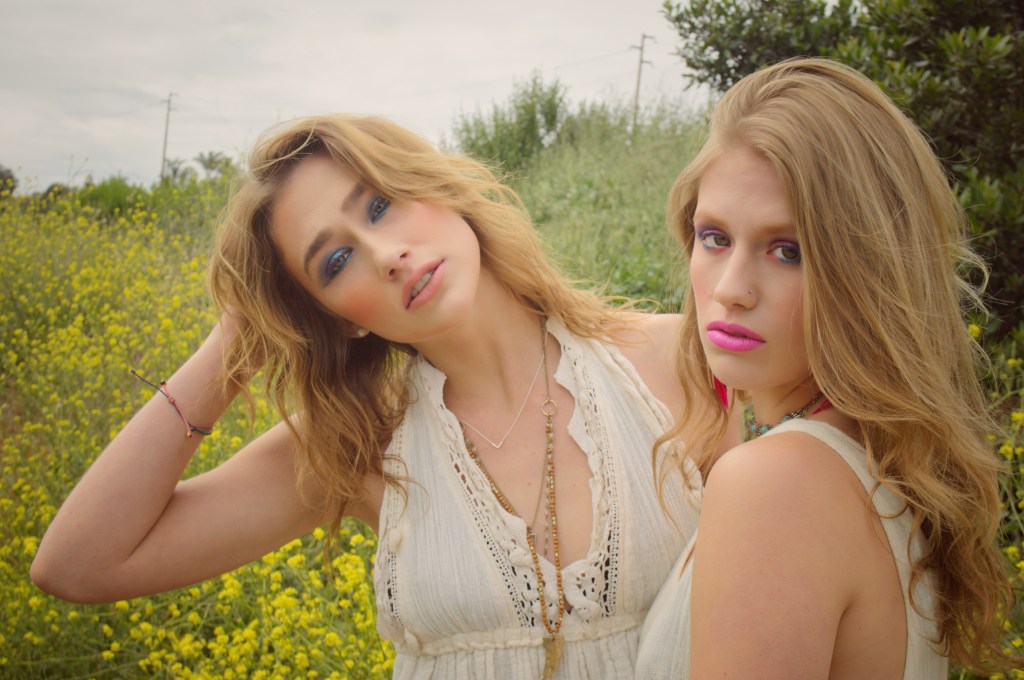 Image of 2 young women with 80’s style makeup with yellow wild flowers