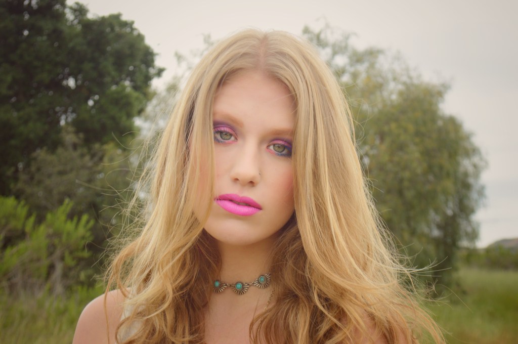 Portrait of a young women with blonde hair standing in front of trees