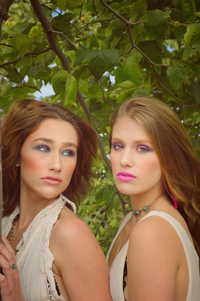 Portrait of 2 young women standing underneath a tree with leaves surrounding them
