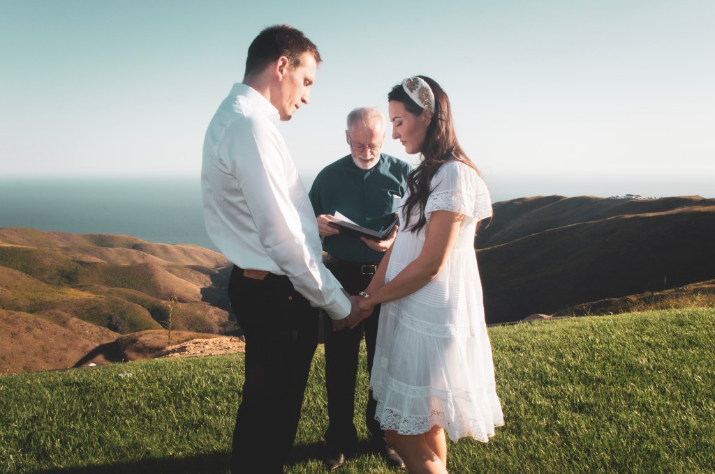 Couple getting married on a mountain side overlooking the ocean