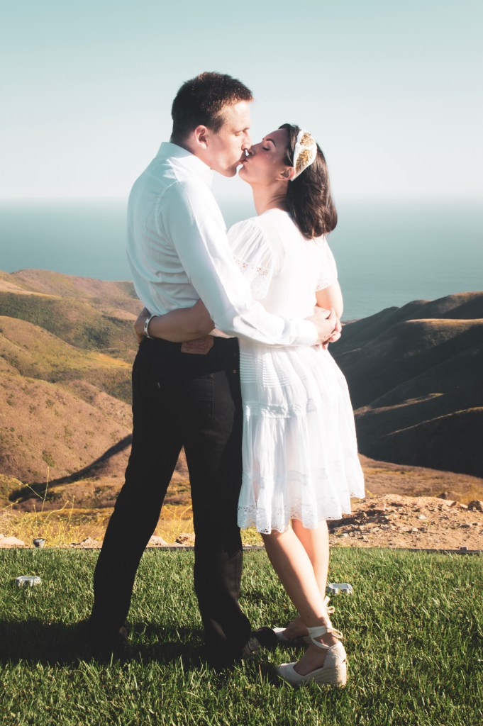 Bride and groom kissing on a mountainside overlooking the ocean