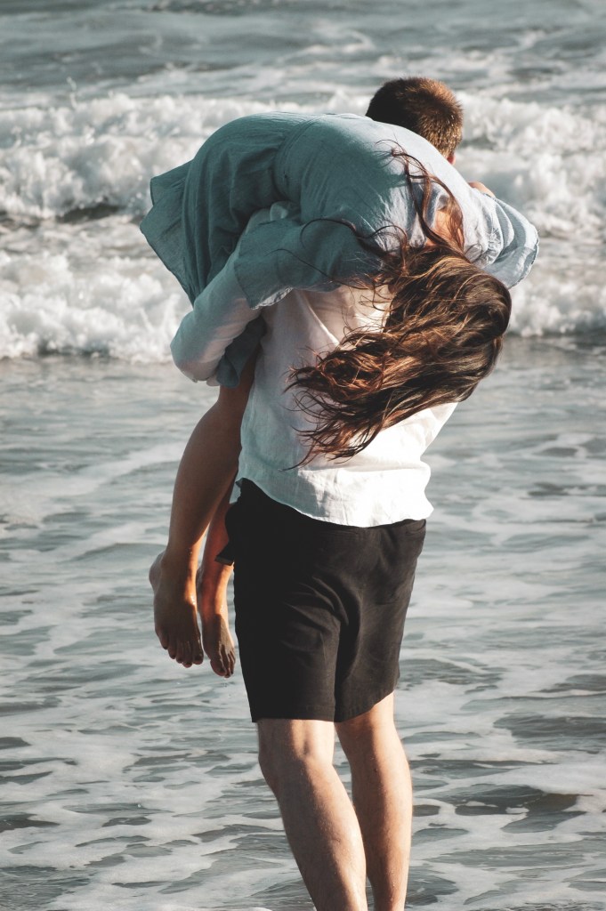 Man with a woman over his shoulder on the beach