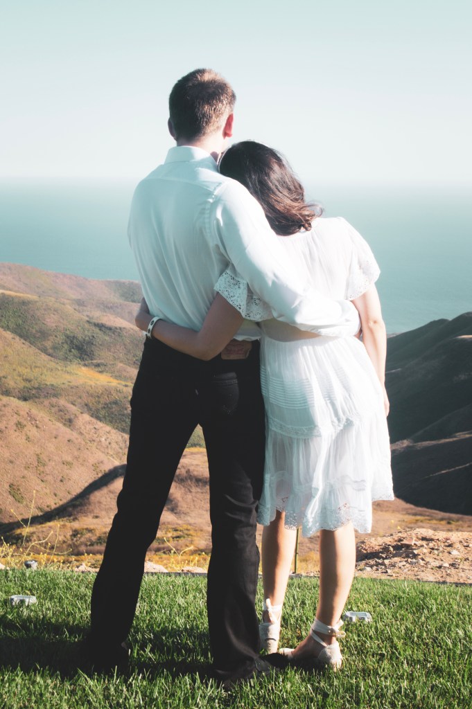 Bride and groom standing side by side hugging looking at the ocean