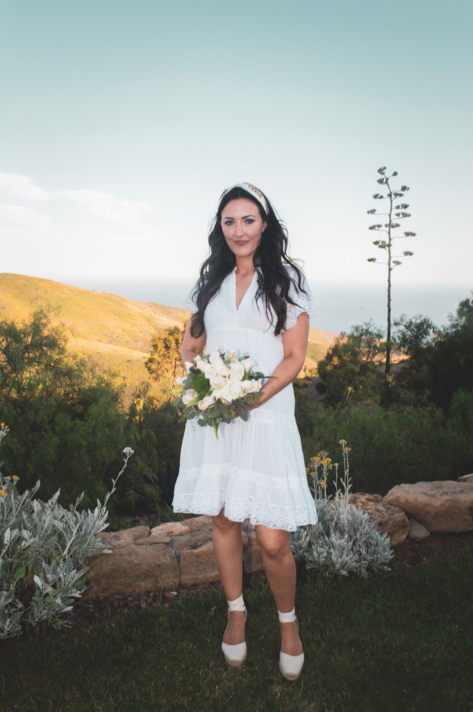 Bride holding white rose bouquet on a mountainside with the ocean view